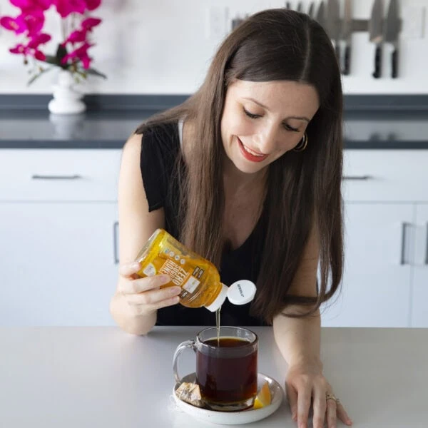 Maya pouring Wholesome Yum original honey into tea.